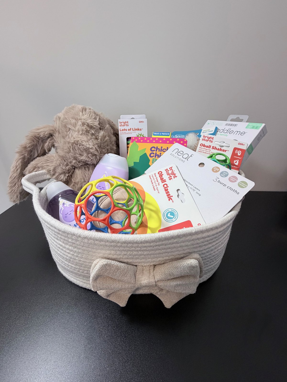 Luxury Collection baby welcome basket with a plush bunny, baby care essentials, toys, and burp cloths in a bow-tied rope basket